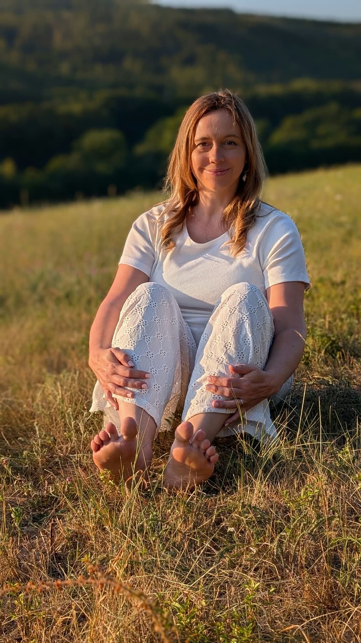Ivana sedí na louce a drží si chodidlo